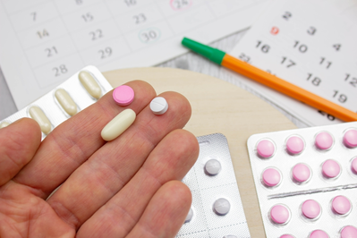 woman holding three different prescription pills over calendar