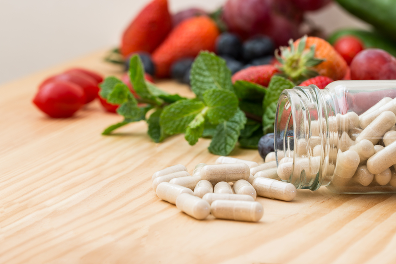 Daily health supplements on counter with fruits and vegetables