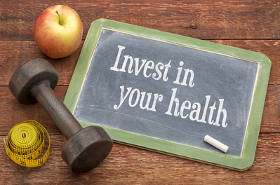 invest in your health written on a chalkboard sign surrounded by workout equipment