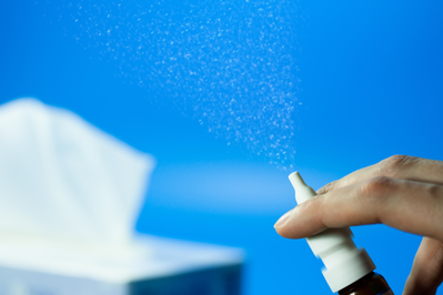 person's hand spraying a nasal spray into the air