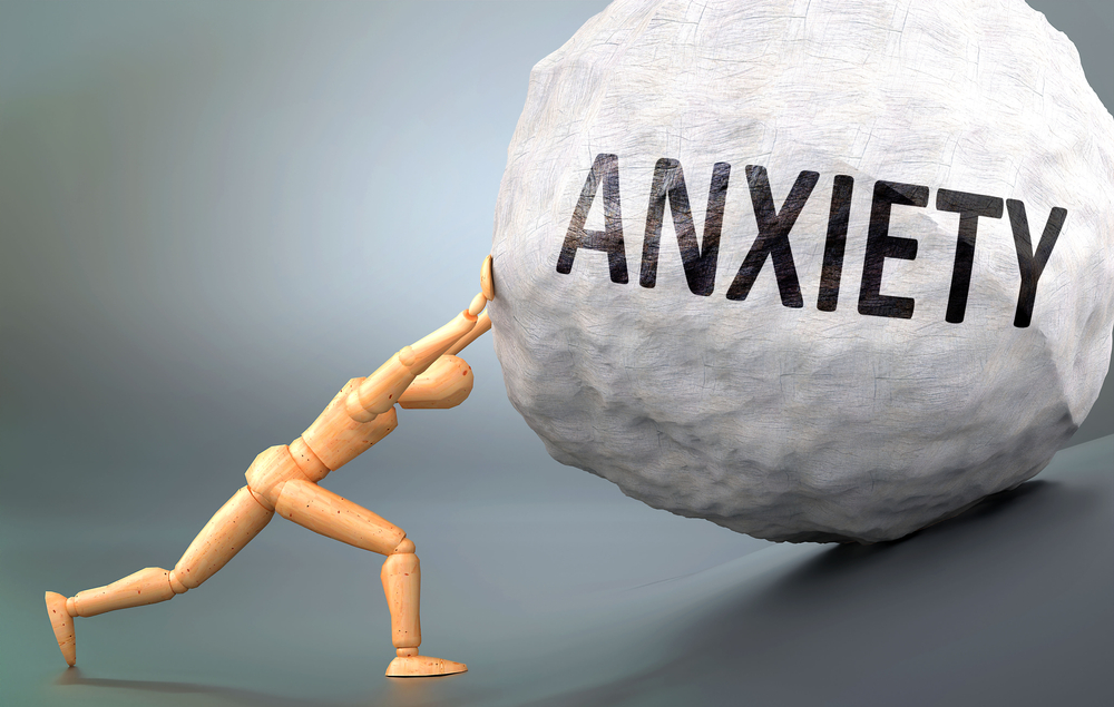 wooden figure pushing a boulder up a hill labeled anxiety