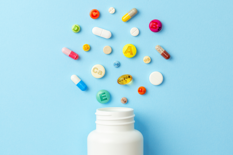 multiple vitamin tablets hovering above a white pill bottle