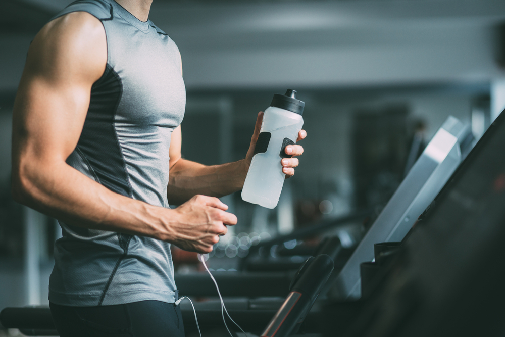 man running on a treadmill while holding a water bottle