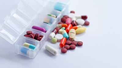 Pill Organizer open to show an assortment of pills of various shapes and colors with a pile of excess pills in front of the container