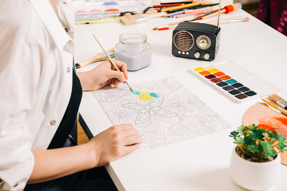 woman sitting at a table painting a coloring page 