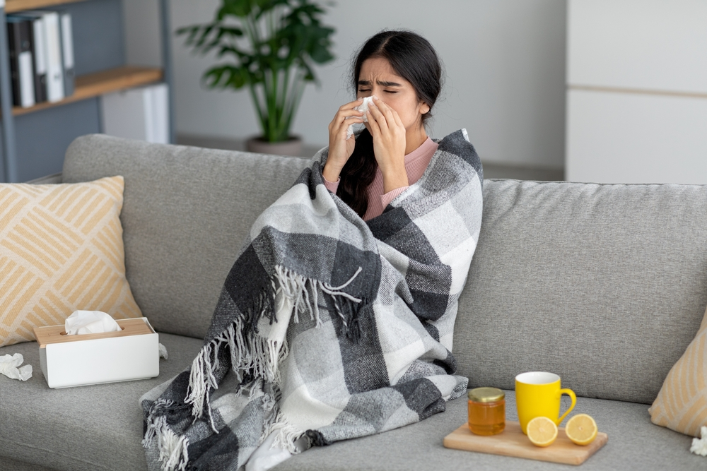 young woman wrapped up in blanket sneezing into tissue