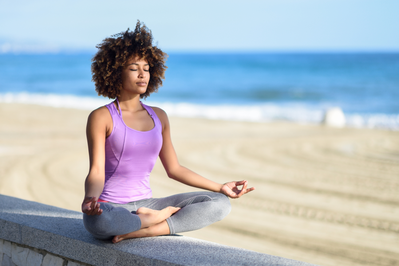 young woman sitting in meditation pose next to the beach