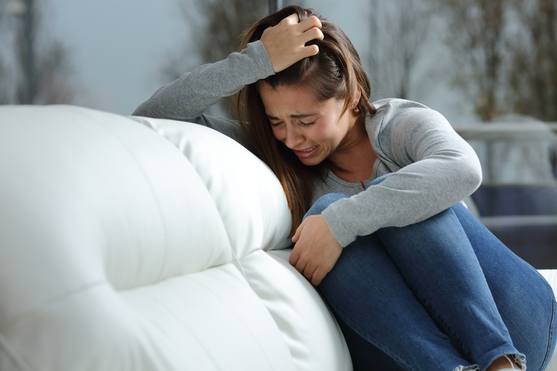 young woman with seasonal depression crying on couch